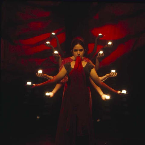 black and red background a young woman with many arms holding small lite candles
