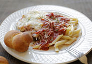 A plate of chicken parm, ziti and a garlic knot with a fork resting on the side of the plate. 