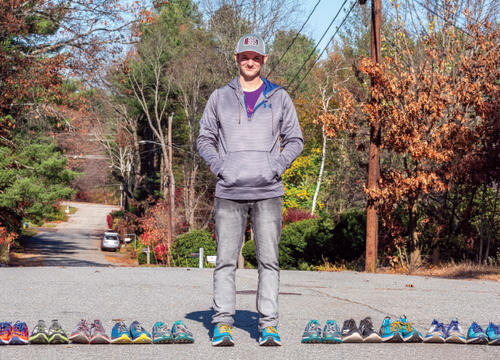 Matty Gregg stands with 31 pairs of sneakers lined up next to him