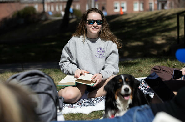 Girl reading a book with a dog on campus