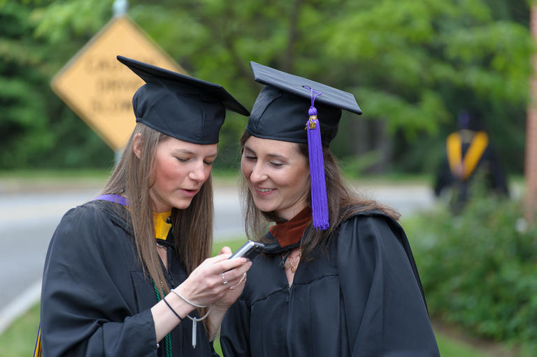 two graduates looking at a cellphone 