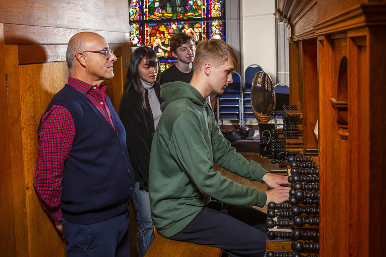 three students and a teacher gathered at an organ