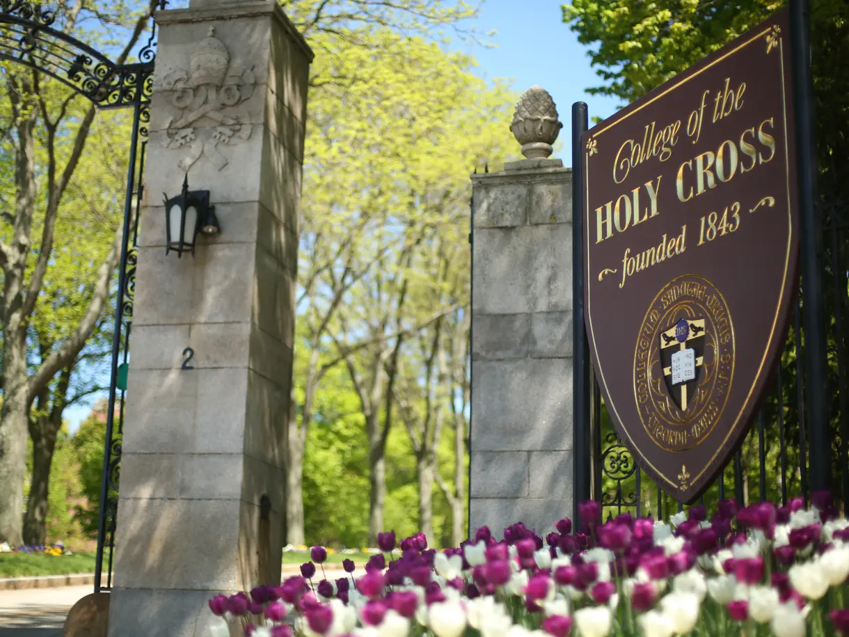 Flowers below a welcome sign that reads "College of the Holy Cross - founded 1843. 