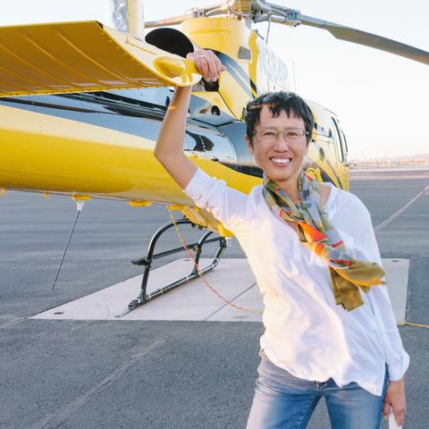 Xu Xi, wearing a white shirt, smiles and leans on a yellow helicopter.