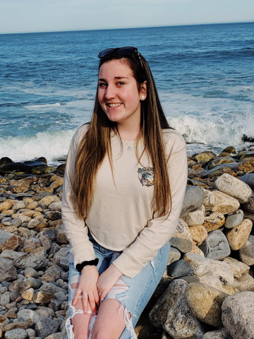 a young woman sitting on the rocks at the beach