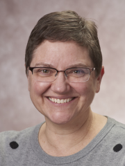 woman in a gray sweater and glasses smiling to camera