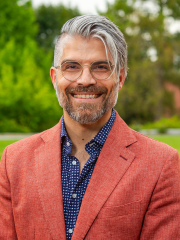 man in a blue shirt and red jacket smiling at the camera